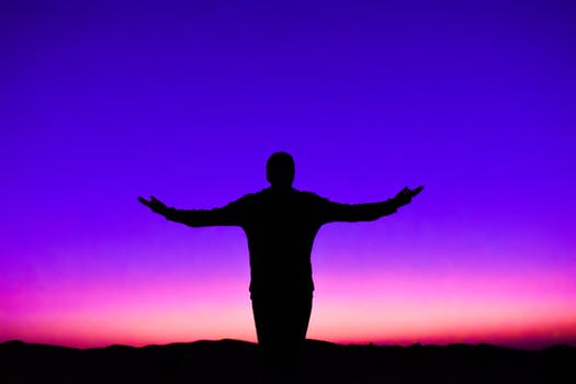Immagine in controluce di una persona con le braccia aperte e le palme delle mani rivolte in alto, su uno sfondo di colori molto accentuati. Nella filosofia di vita rock stoica per la cura di sé i maestri sono coloro i quali hanno messo in pratica personalmente i principi, i valori e le idee da loro diffuse.