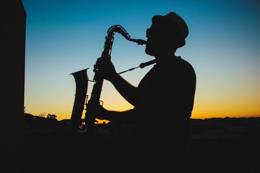 Immagine in controluce di un sassofonista con bombetta sullo sfondo di un tramonto. Nella filosofia di vita rock stoica per la cura di sé le canzoni sono spunti per riflessioni, intuizioni e illuminazioni. La musica rock è una filosofia di vita.