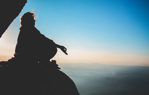 Immagine in controluce di una persona in meditazione su uno spuntone di montagna. La meditazione è una delle componenti del "training" spirituale e filosofico conosciuto come "askesis". Nostri riferimenti sono cose, persone e situazioni in linea con la filosofia di vita rock stoica per la cura di sé.