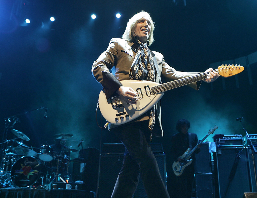 Immagine di Tom Petty, con un grande foulard, ripreso durante un concerto mentre suona una chitarra con la cassa color crema ( “Tom Petty” by Mexicaans fotomagazijn is licensed under CC BY-NC 2.0). La musica rock è una filosofia di vita.