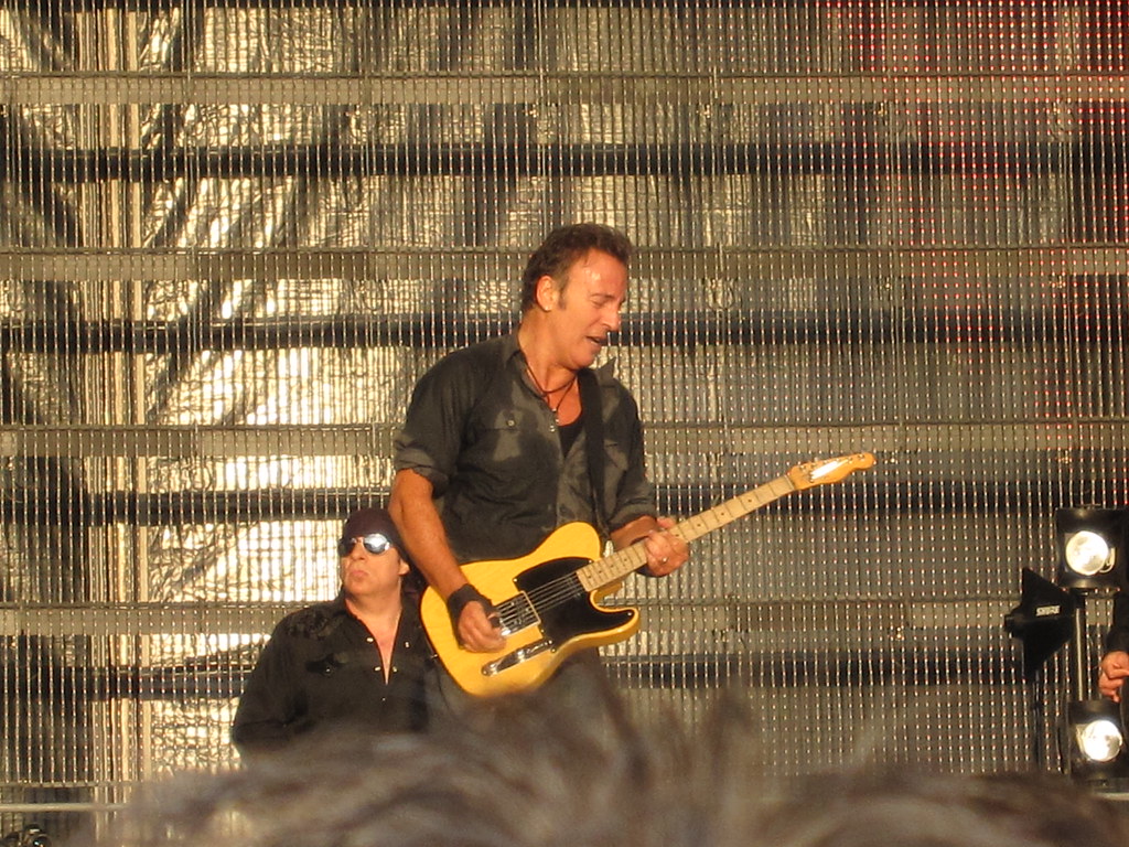 Immagine di Bruce Springsteen ripreso mentre suona una chitarra elettrica gialla su un palcoscenico fortemente illuminato. Alle sue spalle Little Steven con occhiali a specchio. (“IMG_1277” by avonea is licensed under CC BY-NC-ND 2.0). La musica rock è una filosofia di vita.