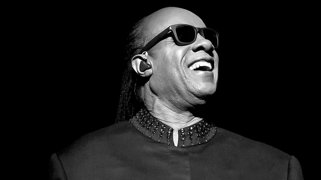 Immagine in bianconero di Stevie Wonder in primo piano sorridente (“Stevie Wonder” by Worlds Direction is licensed under CC0 1.0).