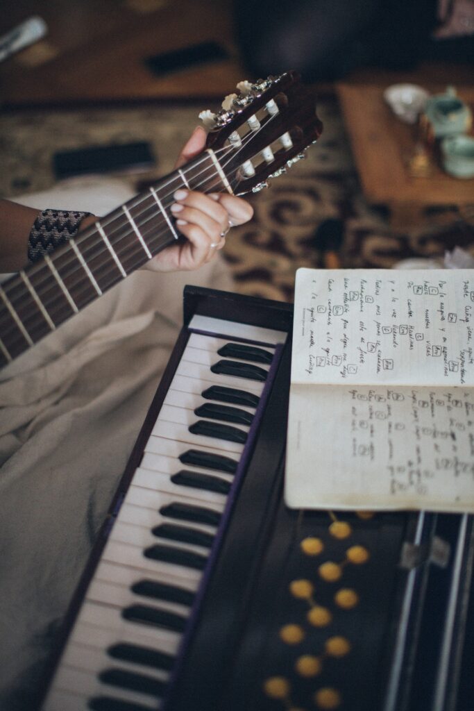 Immagine di un manico di chitarra con una mano che lo impugna davanti a una tastiera musicale e a uno spartito segnato a mano. Filosofia di vita rock stoica vuol dire lavorare sui testi delle canzoni come su libri di filosofi e pensatori. Photo by Elina Sazonova.