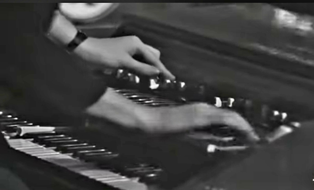 Immagine in b/n di due mani sulla tastiera di uno strumento musicale.