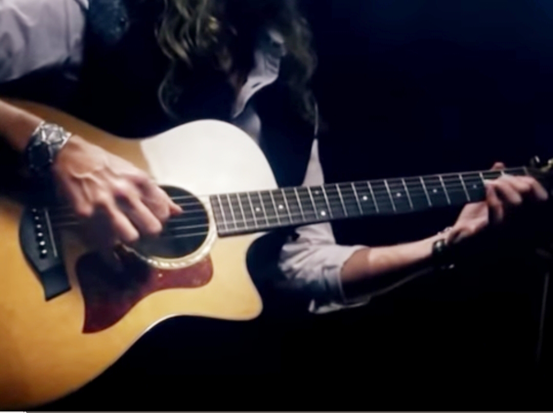 Immagine di una chitarra acustica con le due mani del musicista sulle corde.