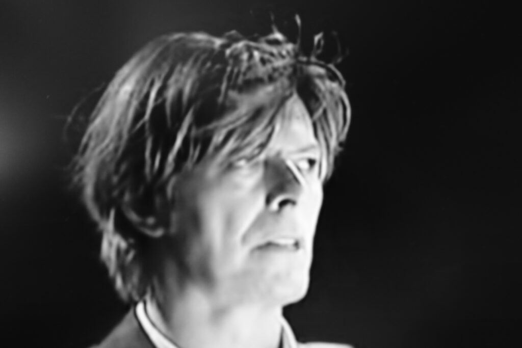 Immagine fotografica in bianconero (primo piano) di David Bowie in concerto.
