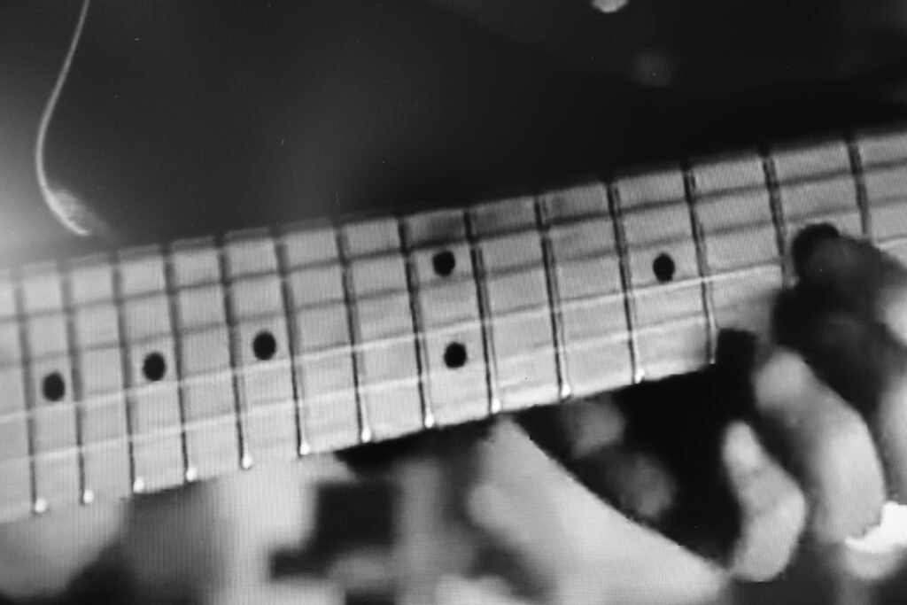 Immagine b/n della tastiera di una chitarra mentre viene suonata.