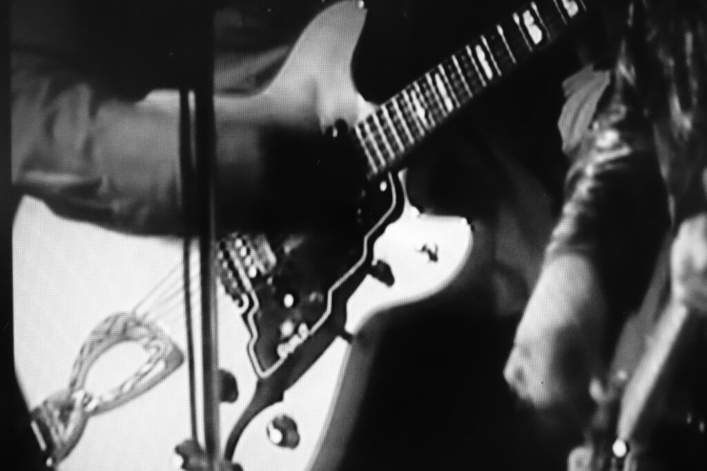 Immagine b/n del manico di una chitarra in primo piano, con una seconda chitarra in secondo piano.