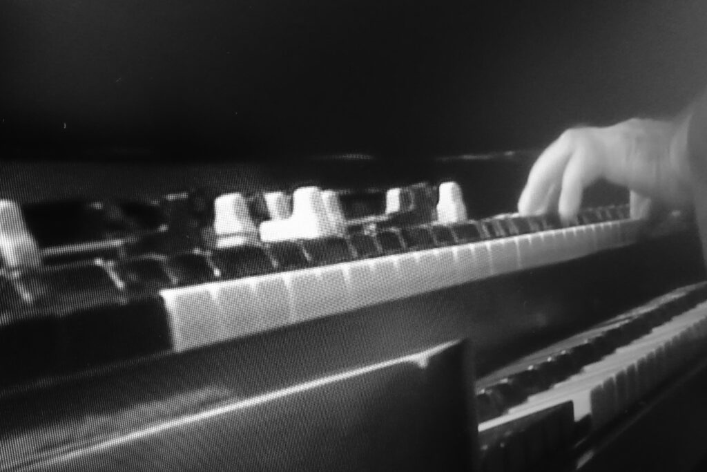 Immagine in b/ di una tastiera musicale su cui si vede una mano che suona.