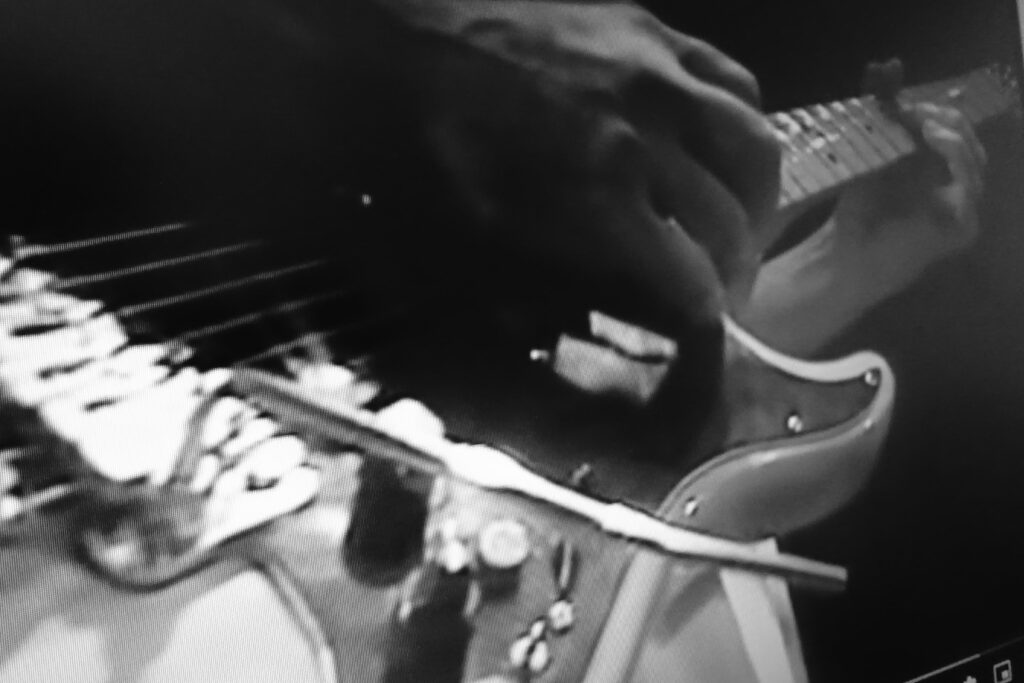 Immagine in b/n di una chitarra in primo piano mentre viene suonata durante un concerto rock.